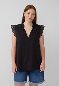 Blouse noire avec un col en V et une bordure en dentelle sur les manches. Tissu doux, coupe décontractée, associée à un short en denim.