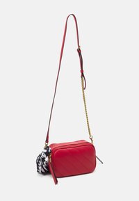 Borsa a tracolla rossa con design trapuntato, catena dorata e cinturino in pelle, con una sciarpa a fantasia bianca e nera attaccata alla zip.