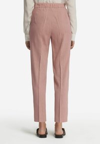 Ljust rosa, högmidjade byxor med avslappnad passform, försedda med veck och en mjuk textur. Fåll avslutad vid ankellängd, parat med platta skor.