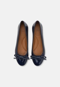 Marineblå patentleather balletflater med rund tå, elastisk kant og en liten sløyfe foran. Innvendig har de glatt tan-fargede fôr.