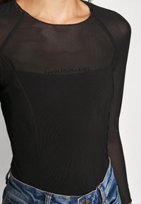 Czarny bodysuit z długim rękawem wykonany z przezroczystej tkaniny, z okrągłym dekoltem i wytłoczonym logo Calvin Klein Jeans z przodu.