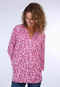 Floral tunic top featuring a pink background with white flowers, v-neckline, long sleeves, and a relaxed fit.