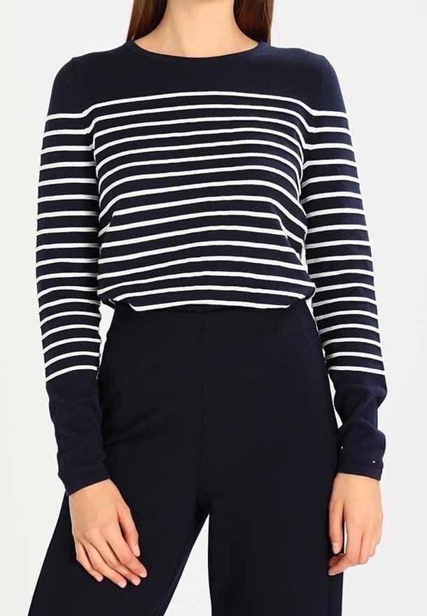 Femme portant un haut à manches longues bleu marine avec des rayures horizontales blanches, associé à un pantalon bleu marine taille haute.