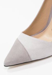 Chaussure à talon haute en suede gris avec un bout pointu ; présente un panneau texturé contrastant à l'avant et un revêtement intérieur lisse.