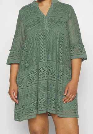 Groene kanten jurk met een V-hals, driekwart mouwen en gedetailleerd ingewikkeld patroon. Heeft een losse, A-lijn vorm en een gestructureerde stof.