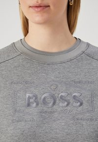 Felpa grigia con logo "BOSS" ricamato e testurizzato. Presenta una scollatura rotonda e una finitura liscia. Nessun altro motivo o dettaglio distinto.