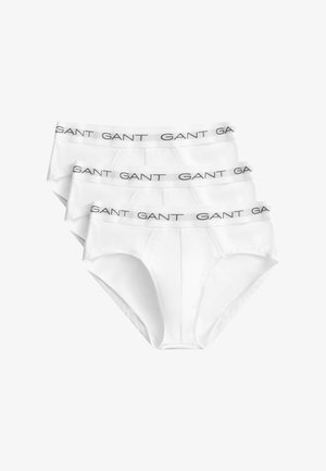 Trois slips blancs pour hommes avec des ceintures élastiques portant le nom de la marque "GANT" en lettres noires.