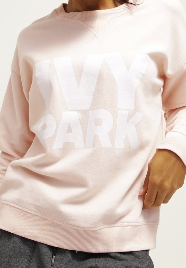 Sudadera rosa claro con gran texto blanco "IVY PARK". Presenta un cuello redondo, puños acanalados y una textura de tela suave.