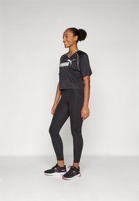 T-shirt de sport noir coupé avec des accents blancs et un logo, associé à un legging noir uni et des chaussures de course noires avec des détails roses.