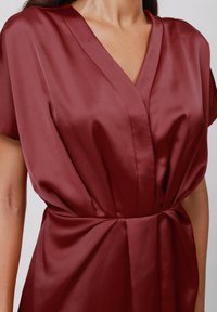 Burgunder satinnedress med dyp V-hals, korte ermer og samlet midje detalj, som viser glatt tekstur og drapert design.