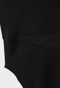 Bodysuit noir en tissu mat lisse avec des panneaux en mesh transparent au niveau de la taille, créant un contraste de textures superposées.