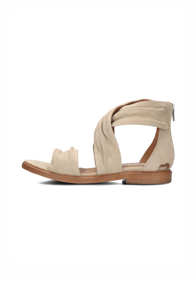 Beige suede sandal with twisted strap design, open toe, flat wooden sole, and a decorative zipper on the back heel.