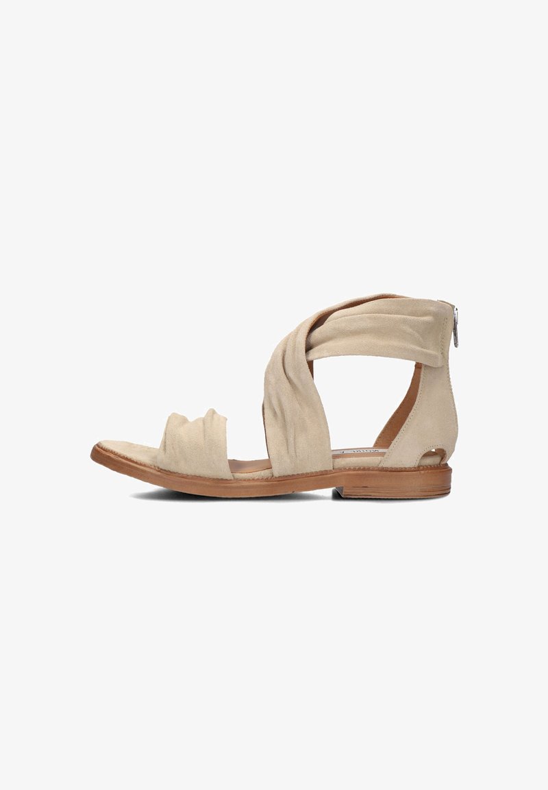 Beige suede sandal with twisted strap design, open toe, flat wooden sole, and a decorative zipper on the back heel.