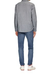 Grijze langemouwen shirt met een button-down kraag, gecombineerd met lichtblauwe spijkerbroek en witte sneakers met rode accenten.