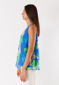Top senza maniche di colore blu in tessuto leggero con un motivo floreale in verde e beige. Vestibilità ampia, scollatura rotonda e texture liscia.