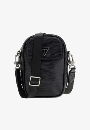 Zwarte gestructureerde schoudertas met verstelbare riem, driehoekig Guess-logo en zilverkleurige sluitingen op witte achtergrond.