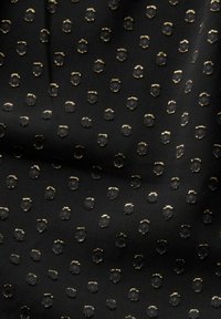 Tissu noir avec de petits points circulaires en relief brodés et soulignés d'or, disposés selon un motif régulier.