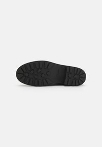 Čierna gumová podrážka topánky s textúrovaným vzorom dezénu a hviezdicovými úchopmi, značková "Clarks" na strane. Okrúly tvar špičky.