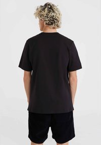 Camiseta de algodón negra con un corte relajado, mangas cortas y un diseño liso, combinada con pantalones cortos de pana azul marino con bolsillos traseros.