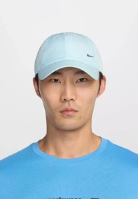 Gorra de béisbol azul claro con visera curvada, hecha de tela. Presenta un pequeño logo negro de Nike en el frente. Textura sencilla y suave.