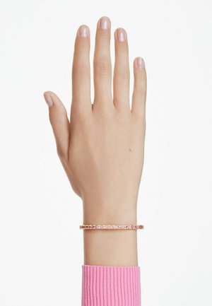 Bracciale in oro rosa con gemme rosa rettangolari, indossato su una mano con pelle chiara; si vedono un bracciale a manica testurizzata e una manica rosa a coste.