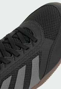 Zwarte sportieve schoen met bovenwerk van mesh, gestructureerde zwarte details en drie grijze strepen. Voorzien van platte veters en een gumrubberen buitenzool.