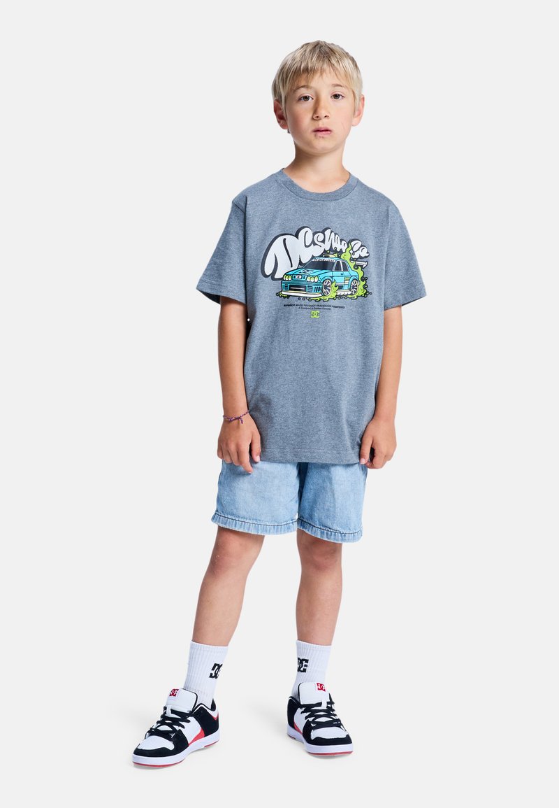 Szara koszulka z kolorową grafiką przedstawiającą samochód, w połączeniu z jasnymi dżinsowymi szortami i czarnymi butami sportowymi z czerwono-białymi akcentami.