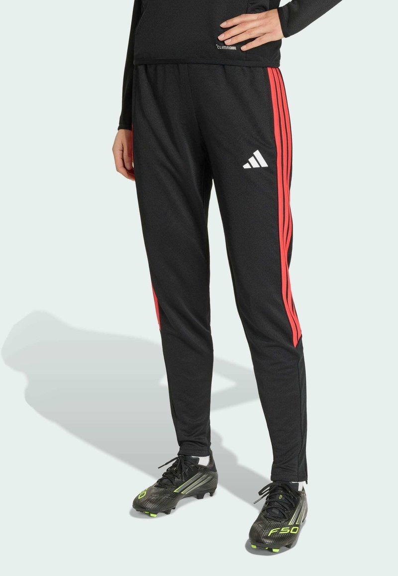 Pantalon de sport noir avec des bandes latérales rouges et un logo adidas. Fabriqué en matière respirante, il possède une taille élastique et des jambes fuselées.