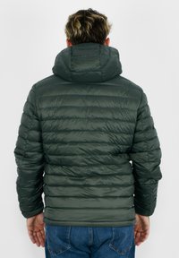 Giacca a vento verde con cappuccio, caratterizzata da un design trapuntato e una trama a costine. La vista da dietro mostra una forma aderente e una finitura liscia.