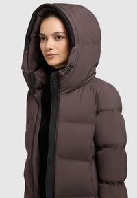 Puffet jacket i dæmpet lilla med en stor hætte, der har en frontlynlås og sort trim. Glat tekstur med quiltede sektioner til isolering.