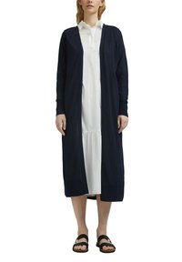 Marineblauer langer Cardigan aus leichter Stoffqualität, mit offenem Vorderteil, langen Ärmeln und gerippten Bündchen, über einem weißen Kleid getragen.