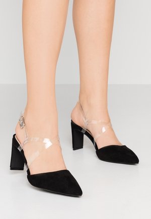 Sorte ruskind højhælede sko med klare stropper og spidst tådesign. Firkantet hæl og spænde detaljer på ankelstropperne.