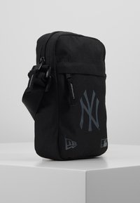 Borsa a tracolla nera in tessuto con chiusura a zip, caratterizzata da un grande logo grigio "NY" e da sottili dettagli di branding sul lato.