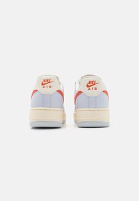 Baskets Nike Air avec une tige synthétique bleu clair, des accents orange, une semelle intermédiaire crème et une semelle en caoutchouc grise. Silhouette classique à coupe basse.