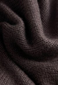 Tissu texturé brun foncé, présentant une surface douce et légèrement duveteuse avec un motif tissé, exhibant des plis et des ombres.
