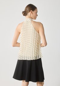 Pleated halter top in light cream with black polka dots. Sheer fabric and high neckline. Black flared skirt completes the outfit.