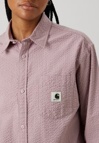 Ljusrosa, texturerad långärmad skjorta med knappkrage, som har en ficka på vänster bröst och en diskret Carhartt-logotag.
