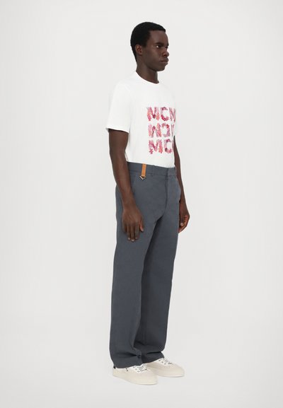 T-shirt blanc avec un texte graphique rouge et rose, associé à un pantalon large gris foncé avec un accent en cuir marron près de la taille.