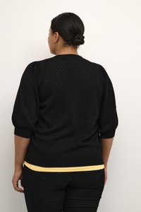 Pull en tricot noir avec des manches bouffantes, présentant un motif texturé et un ourlet côtelé. Superposé sur un haut jaune clair.