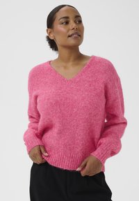 Suéter oversize de cuello en V en color rosa brillante, hecho de hilo esponjoso. Cuenta con puños y dobladillo acanalados, con un ajuste relajado y textura suave.