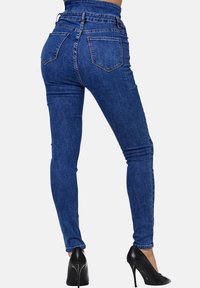 Jeans de mezclilla azul ajustados que presentan una cintura alta, cinco bolsillos y una textura suave, combinados con tacones negros de punta.