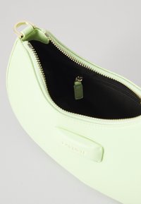 Zelena sintetička torbica sa zaobljenim oblikom, zatvaranjem na zip i zlatnim metalnim detaljima. Unutrašnjost sadrži crnu podstavu i malu zip pohranu.