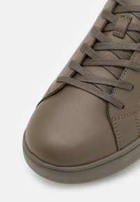 Olivově zelené ko�žené tenisky s kulatou špičkou, tónovými tkaničkami a jemným prošíváním. Hladký povrch s minimalistickým designem.