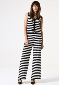 Conjunto de dos piezas a rayas en blanco y negro con una blusa sin mangas que presenta un cierre de lazo y pantalones de pierna ancha, fabricado con tejido texturizado.