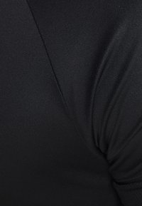 Svart tyg i nära bild, med en jämn textur och subtil lyster. Materialet verkar lätt med svängda sömmar och draperade detaljer.