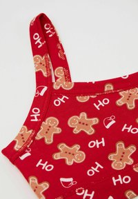 Červený top z látky s opakujícím se vzorem perníkových panáčků a vánočních motivů; tenká ramínka; hladká textura; elastické švy.