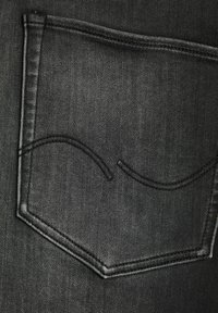 Tela de mezclilla negra con un bolsillo trasero que presenta un patrón de costura curvo. La textura parece suave y ligeramente reflectante.