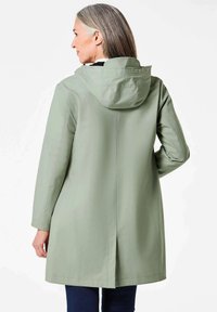 Lichtgroene waterdichte jas met een capuchon, lange mouwen en een rechte snit. Bevat verticale naden en een ventilatieopening bij de achterkant van de zoom.