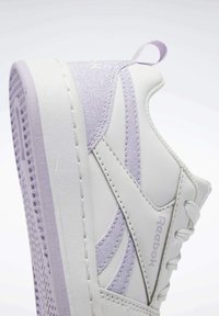 Vita och lavendel Reebok-sneakers med glittrande detaljer, framträdande sula och dragflik på hälen mot en enkel ljus bakgrund.