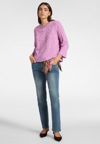 Fioletowy sweter w splot warkoczowy z rękawami do łokcia, połączony z jasnoniebieskimi prostymi dżinsami i wzorzystym szalikiem przewiązanym w talii. Brązowe baleriny.